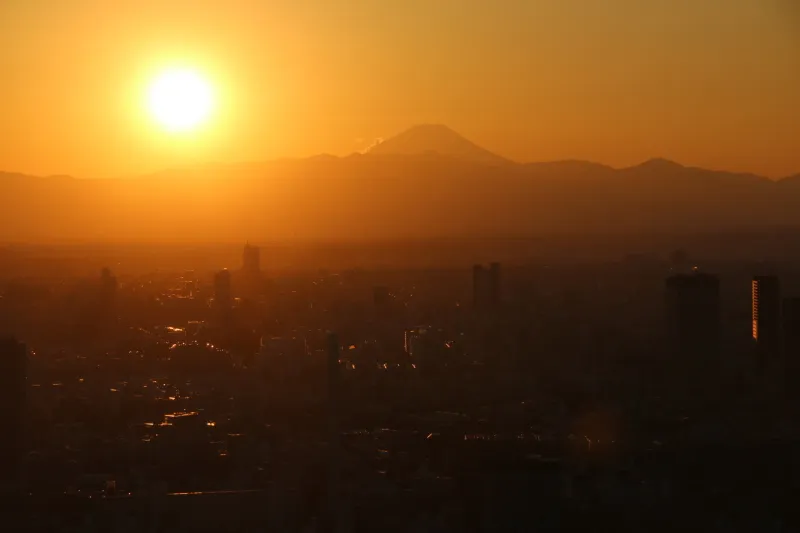 富士山の横に太陽が沈みビルや街並みを赤く照らす夕焼け